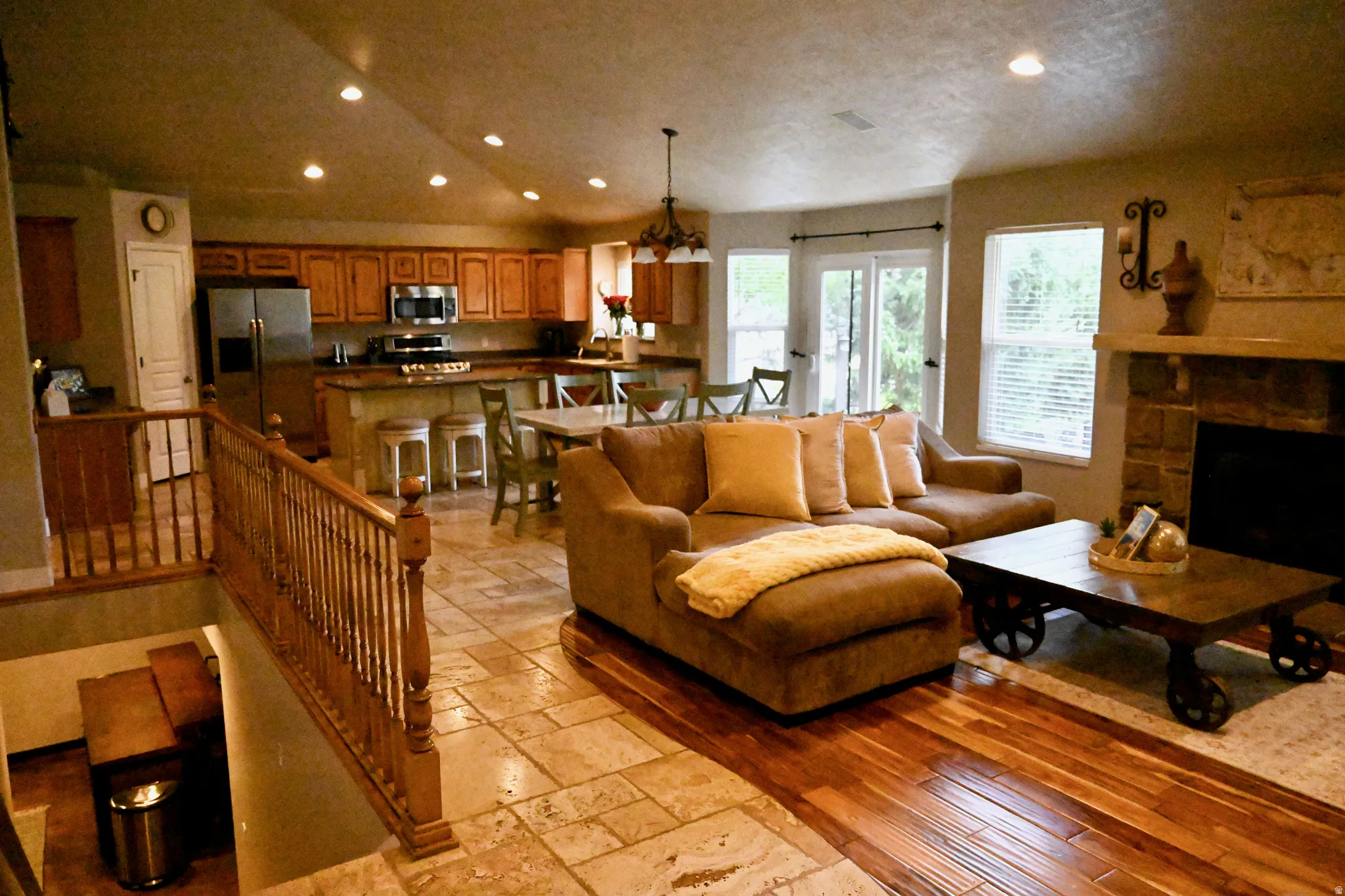 Open-concept living space featuring wood-finish flooring, stone tile flooring, a stone-surround fireplace with a mantel, and recessed lighting