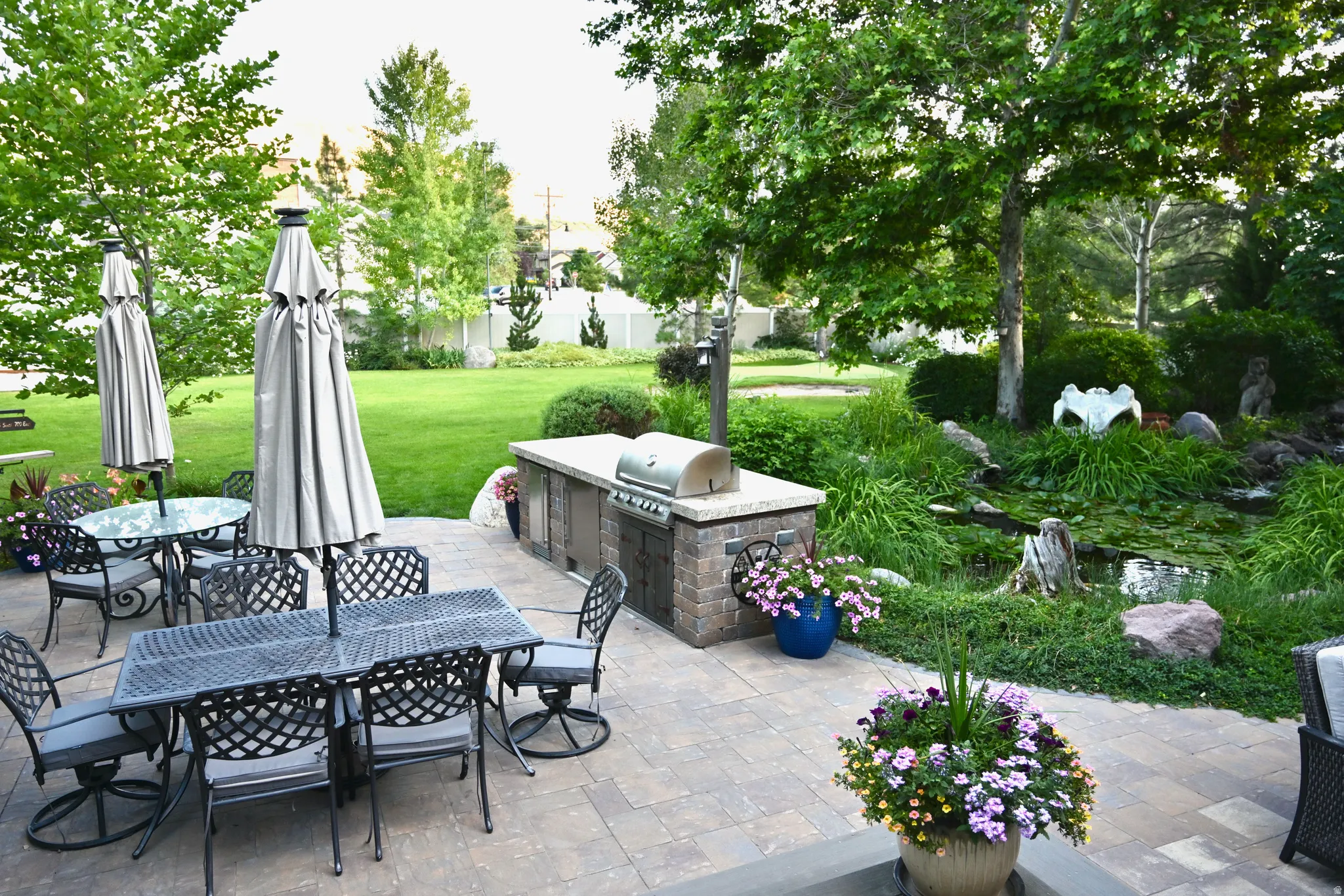 Expansive outdoor patio featuring paver stones, a built-in outdoor kitchen with a grill, and a tranquil water feature