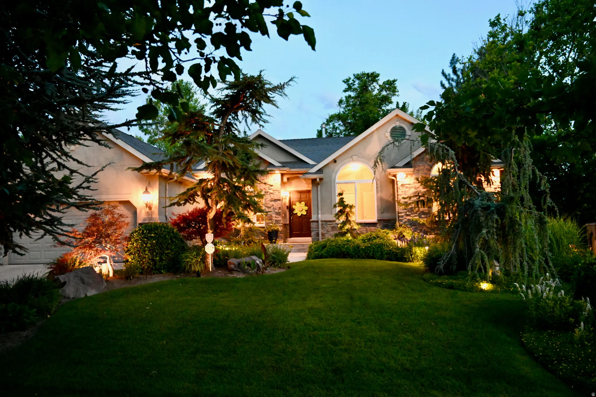 Stucco and stone facade with an arched window, a two-car garage, and meticulously maintained landscaping