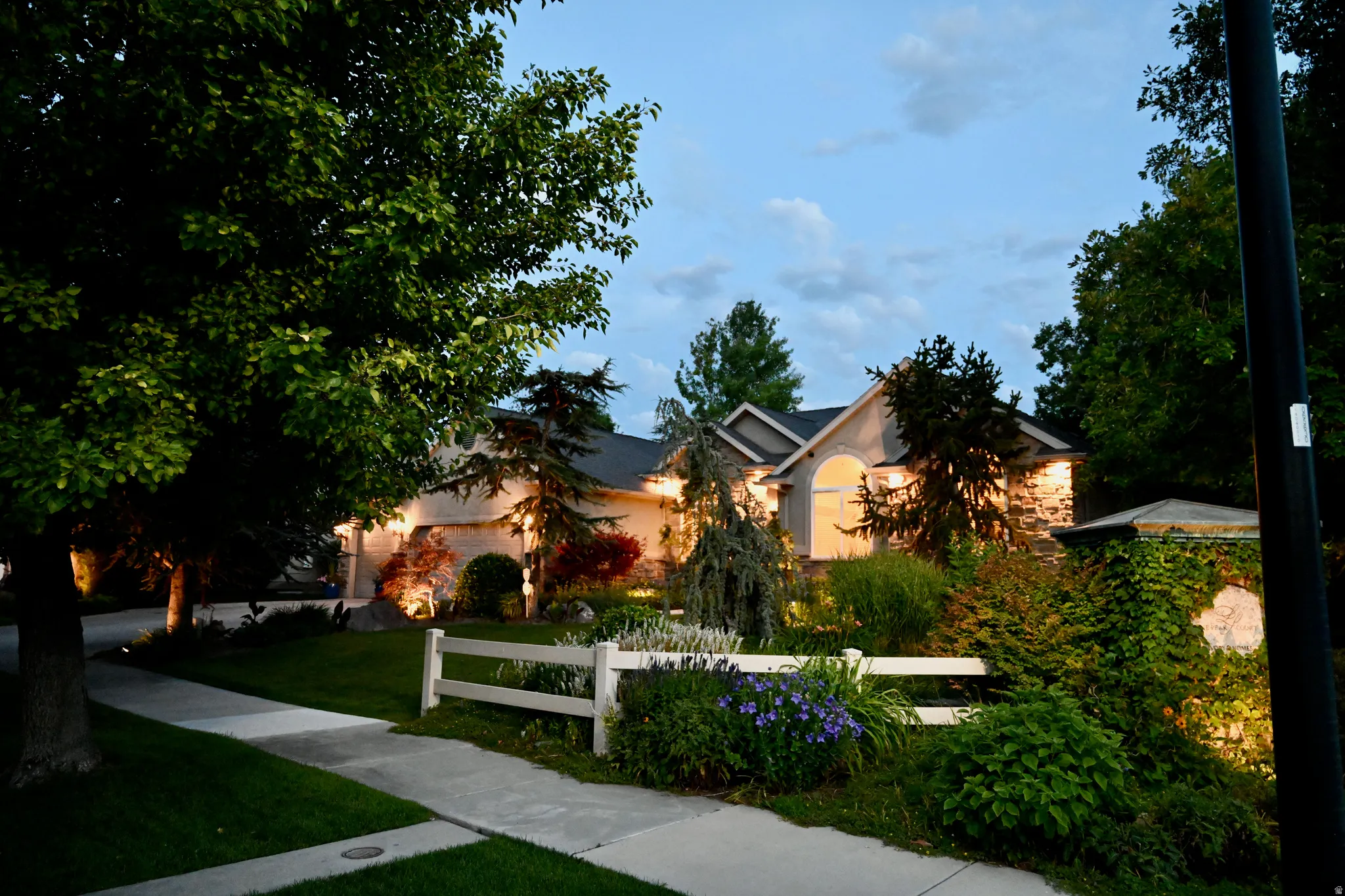 Exterior residence featuring a stucco facade with stone accents, mature landscaping, a curved window, and a white picket fence
