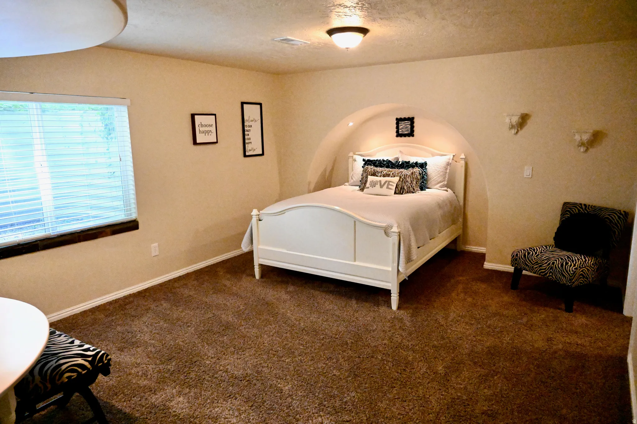 Carpeted room featuring an arched alcove with recessed lighting, a ceiling-mounted light fixture, and a window with horizontal blinds and a dark wood sill