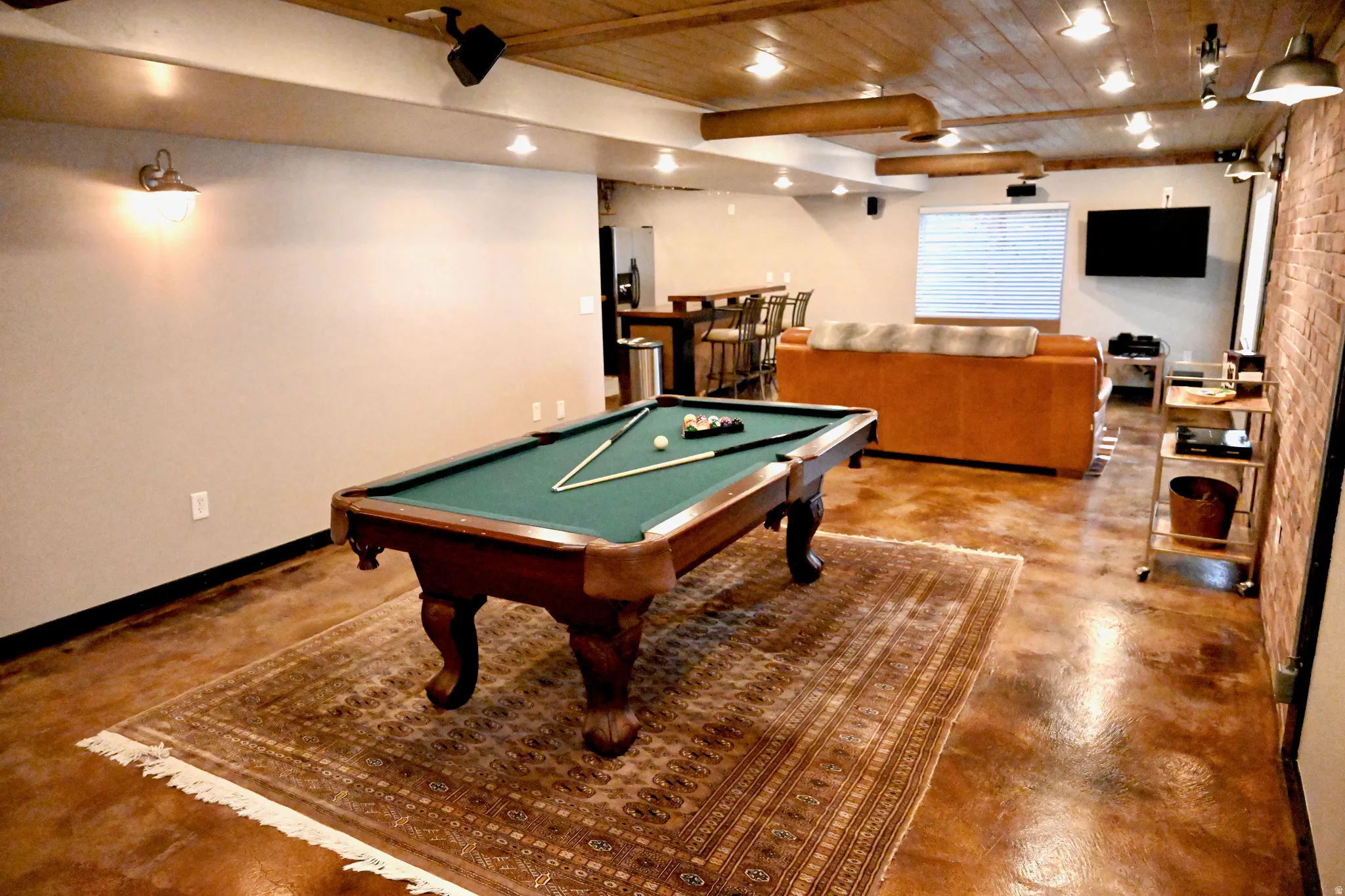 Spacious entertainment area featuring wood-finish flooring, a beamed wood ceiling, and exposed brick accents