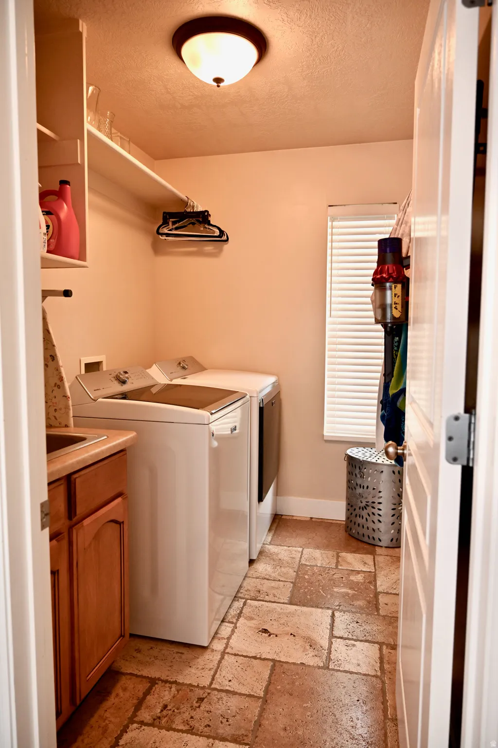 Dedicated laundry area featuring a utility sink, wood cabinetry, and a window with blinds