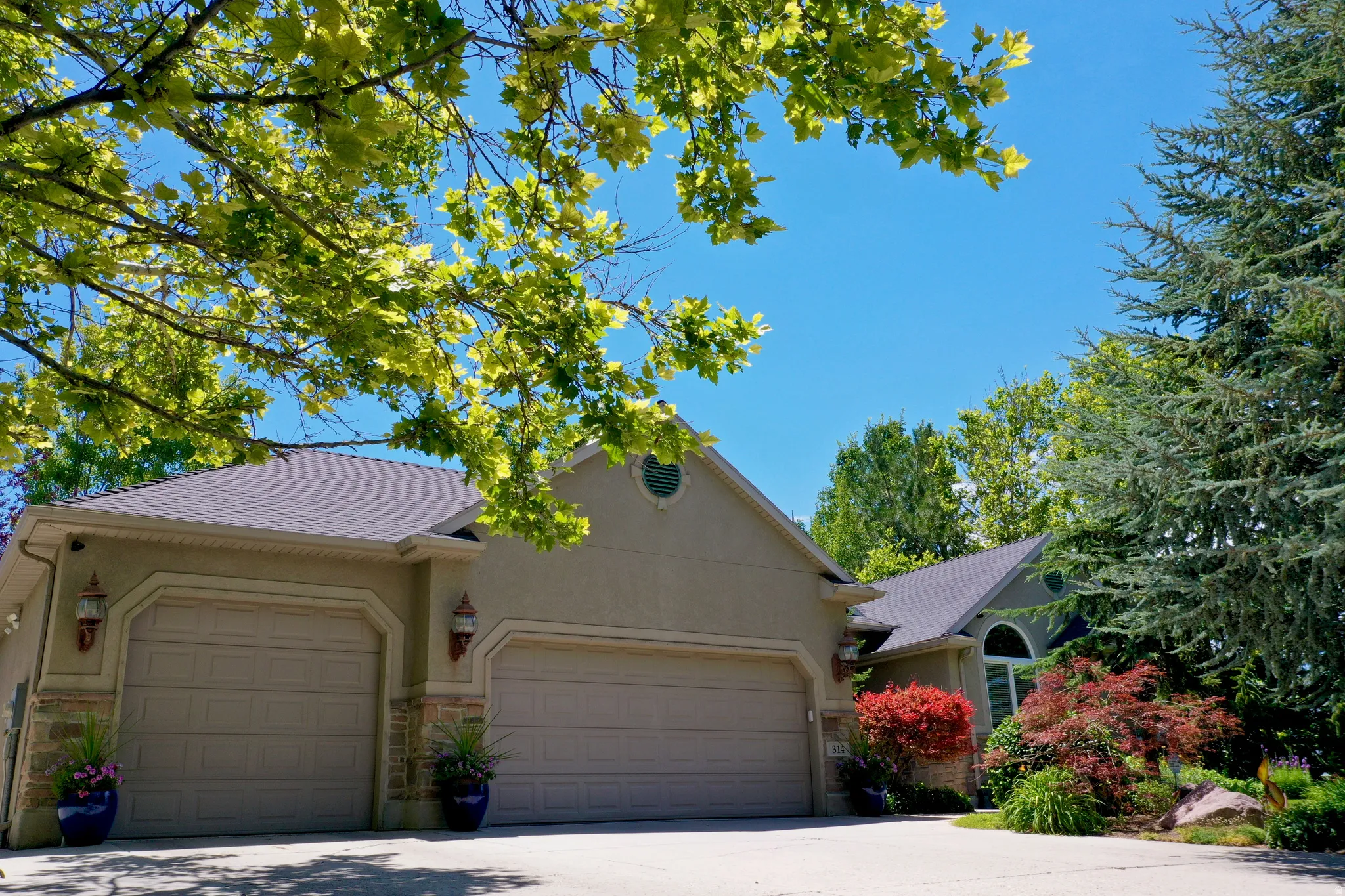 Stucco exterior featuring a dual garage, stone accents, and mature landscaping