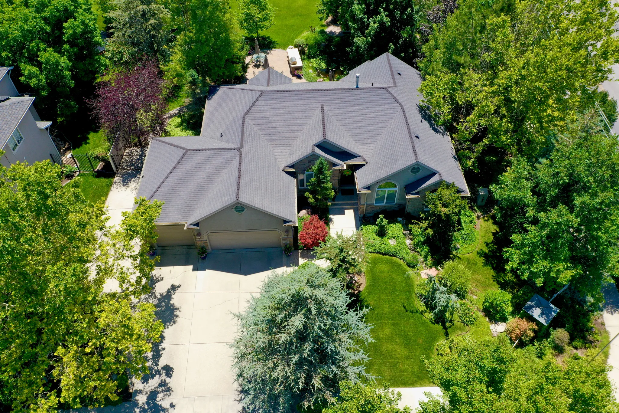 Contemporary residence featuring a multi-gabled roofline, an attached two-car garage, extensive concrete driveway, and mature landscaping with varied foliage