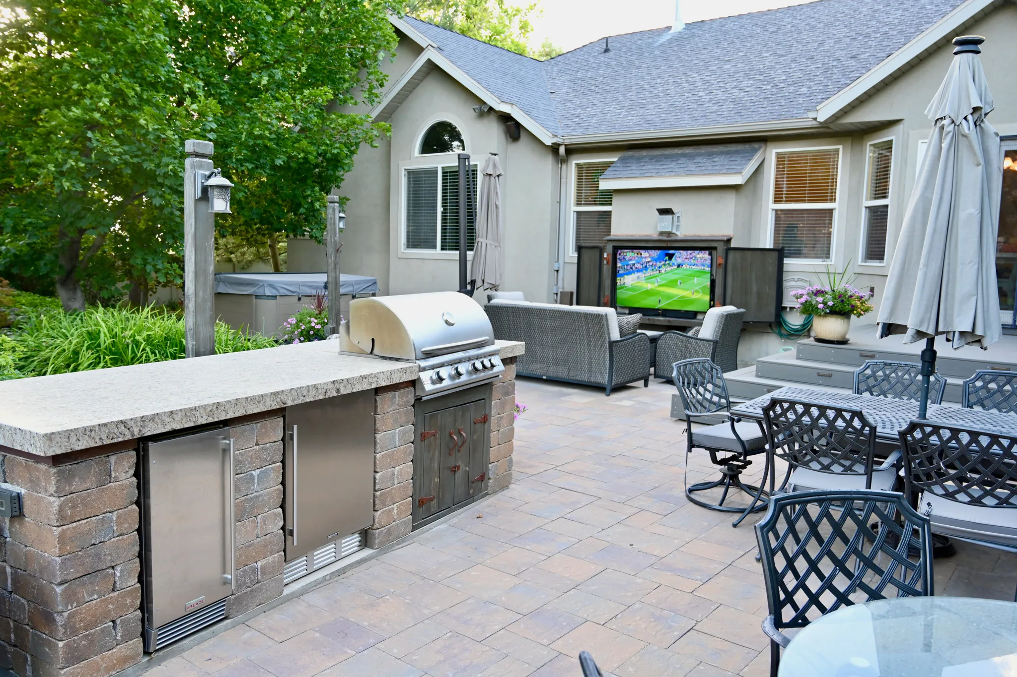 Expansive paver patio featuring a built-in outdoor kitchen with grill and stainless steel appliances