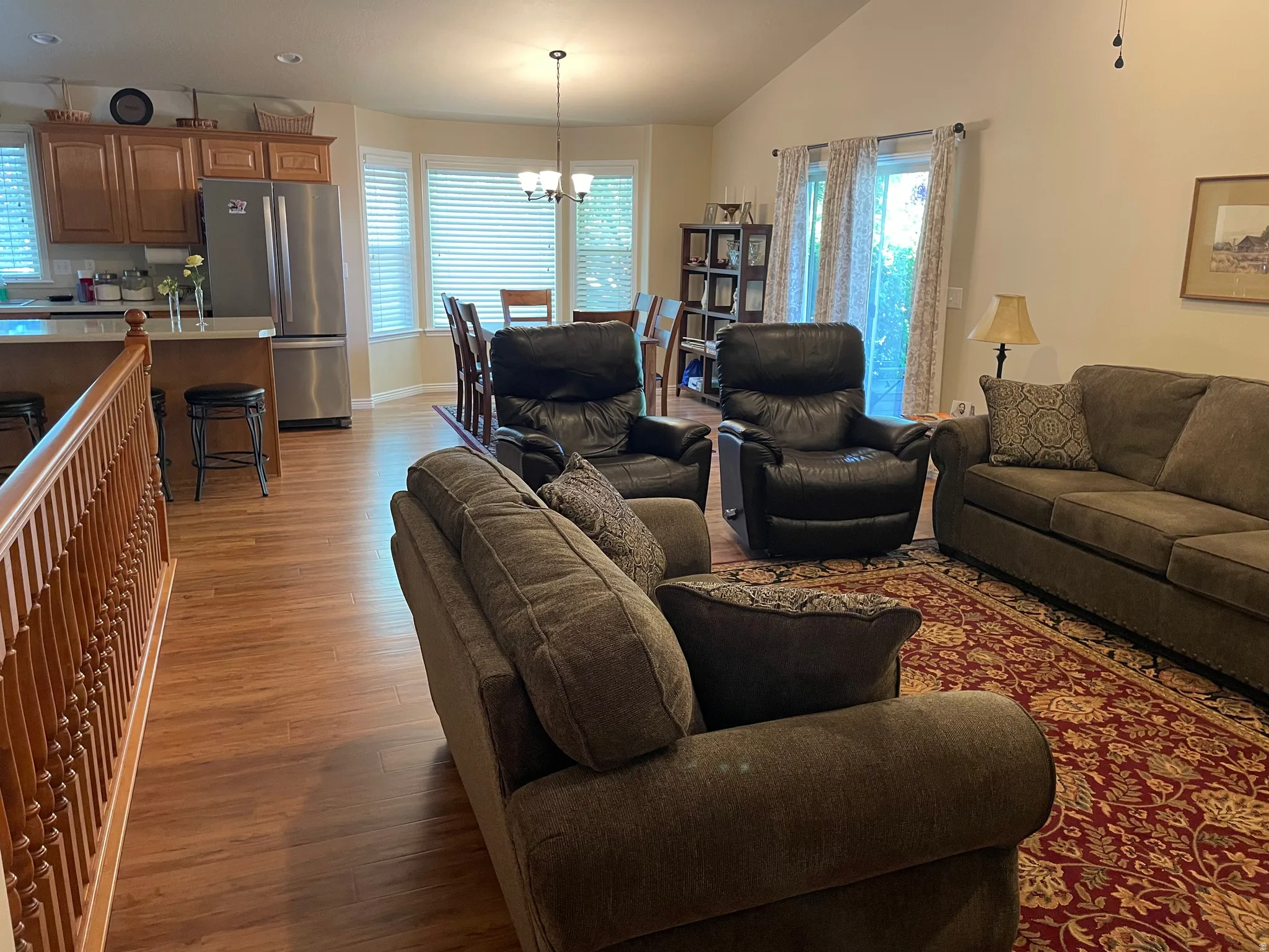 Open-concept living area featuring wood-finish flooring, a kitchen island with seating, natural wood cabinetry, stainless steel refrigerator, and a dining area with bay windows