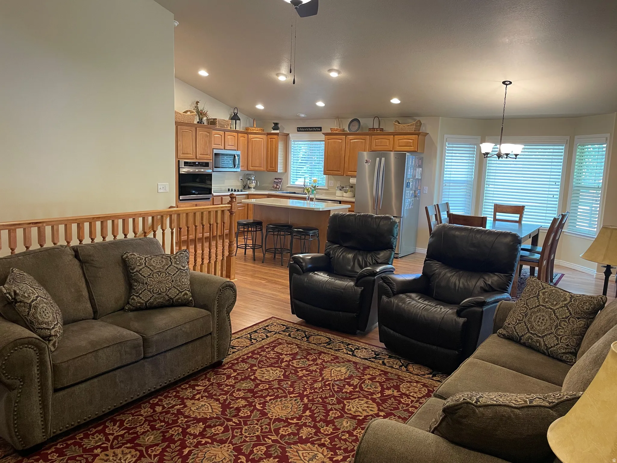 Open-concept living area featuring wood-finish flooring and a kitchen with stainless steel appliances, wood cabinetry, and an island with counter seating