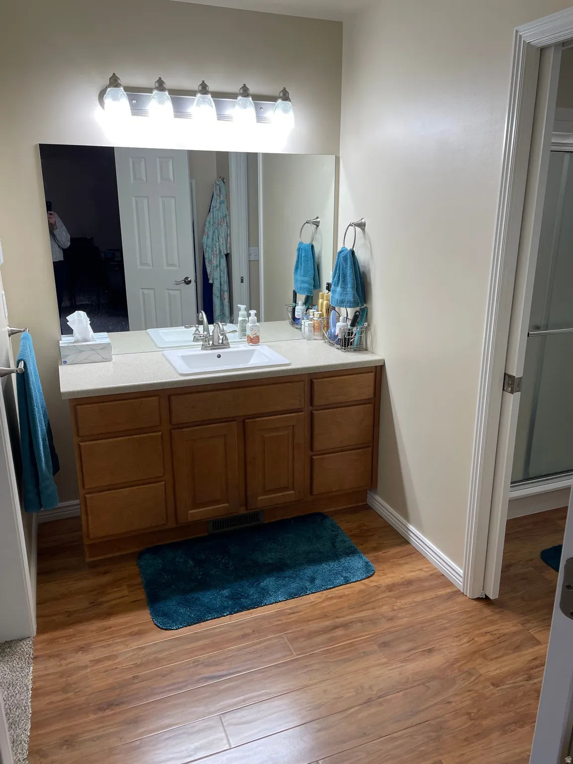 Wood-finish flooring throughout the bathroom, featuring a light-toned wood vanity with a white countertop and integrated sink