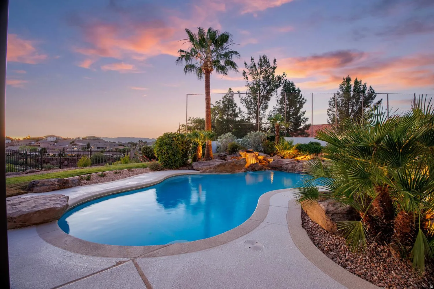 Freeform swimming pool with a rock waterfall feature, integrated spa, and concrete decking