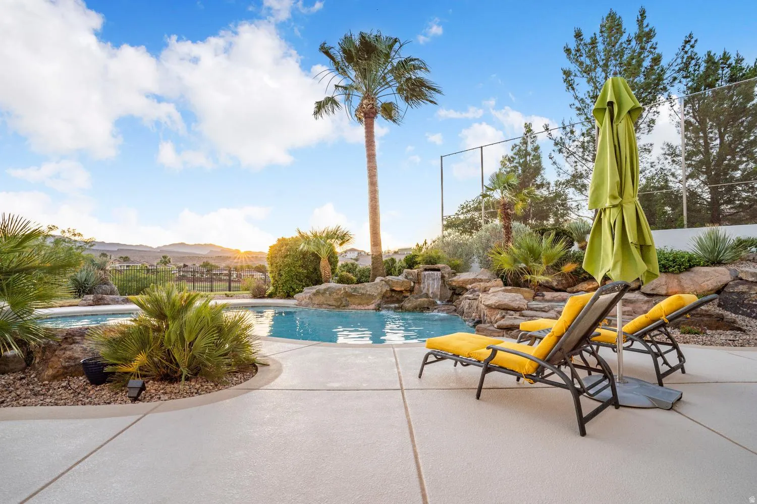 Resort-style pool with rock waterfall feature, integrated spa, and expansive paved decking