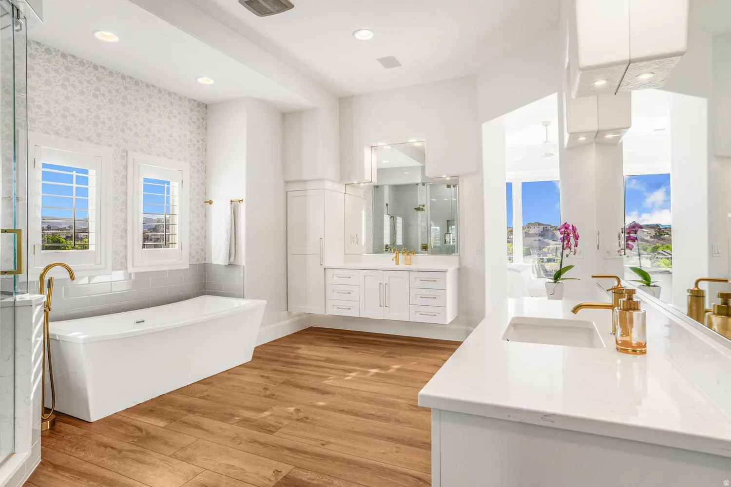 Contemporary bathroom featuring a freestanding soaking tub, dual floating vanities with undermount sinks, quartz countertops, and wood-finish flooring