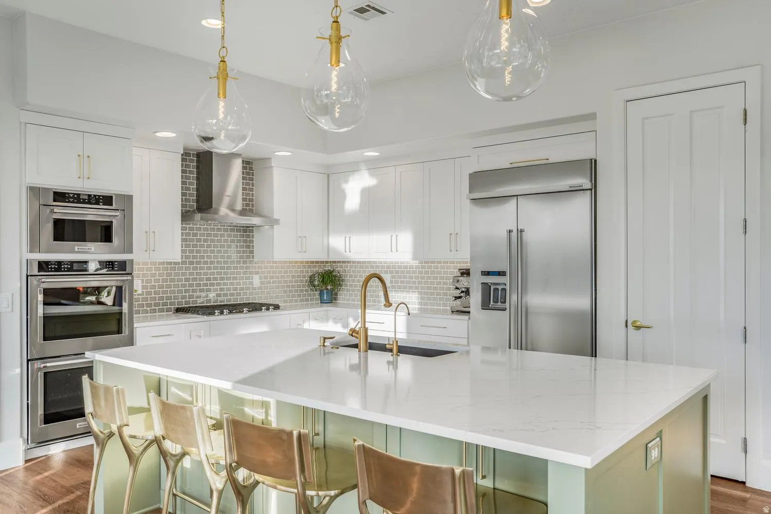 Contemporary kitchen featuring a large center island with a light-toned countertop, white cabinetry, integrated stainless steel appliances, a tile backsplash, and decorative pendant lighting