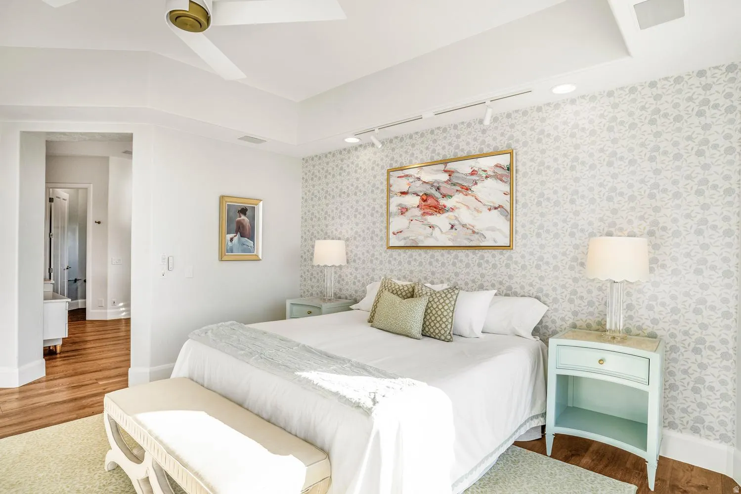 Bedroom featuring patterned accent wall, recessed ceiling with fan, track lighting, and wood-finish flooring