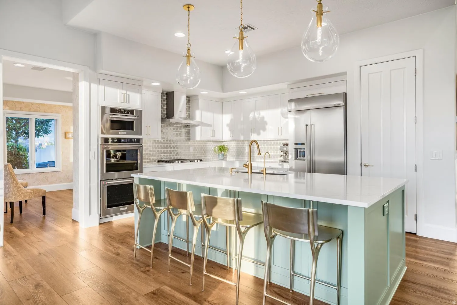 Contemporary kitchen featuring a light green island with a white countertop, gold-toned pendant lighting, stainless steel appliances, white cabinetry, and wood-finish flooring
