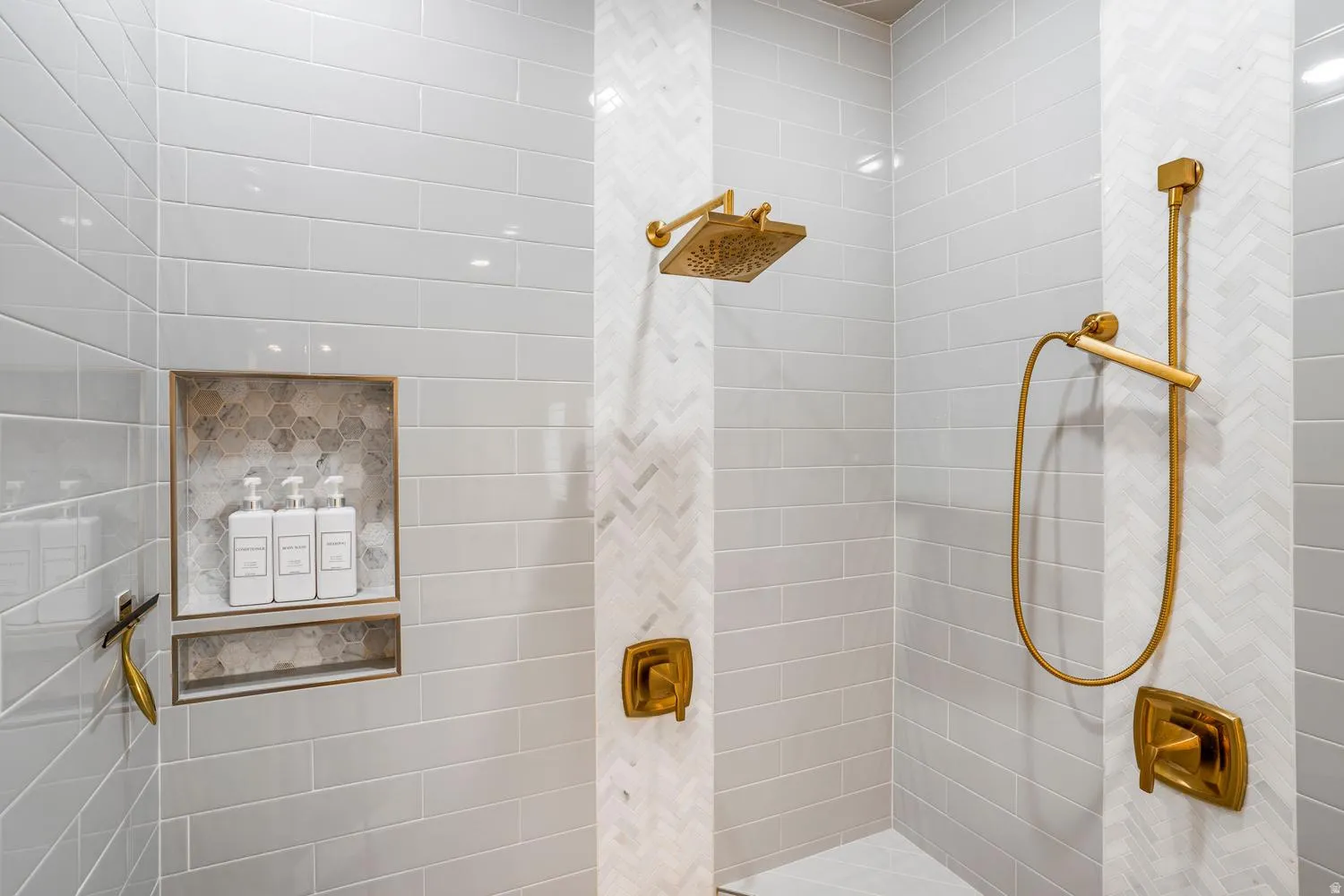 Shower enclosure featuring light gray subway tile walls and herringbone pattern accent tile