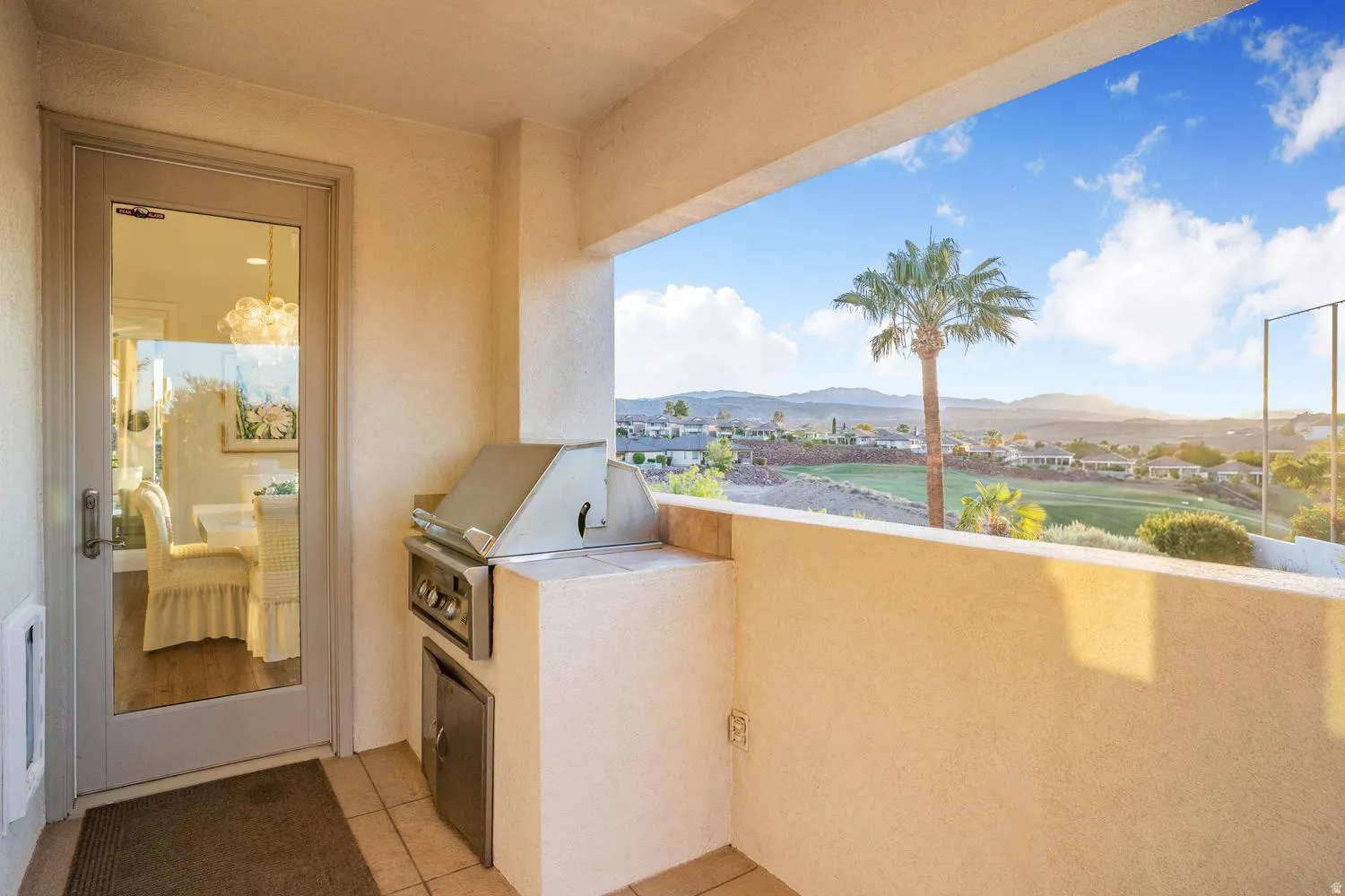 Outdoor balcony featuring a built-in stainless steel grill with integrated storage, tile flooring, and a glass-paneled door