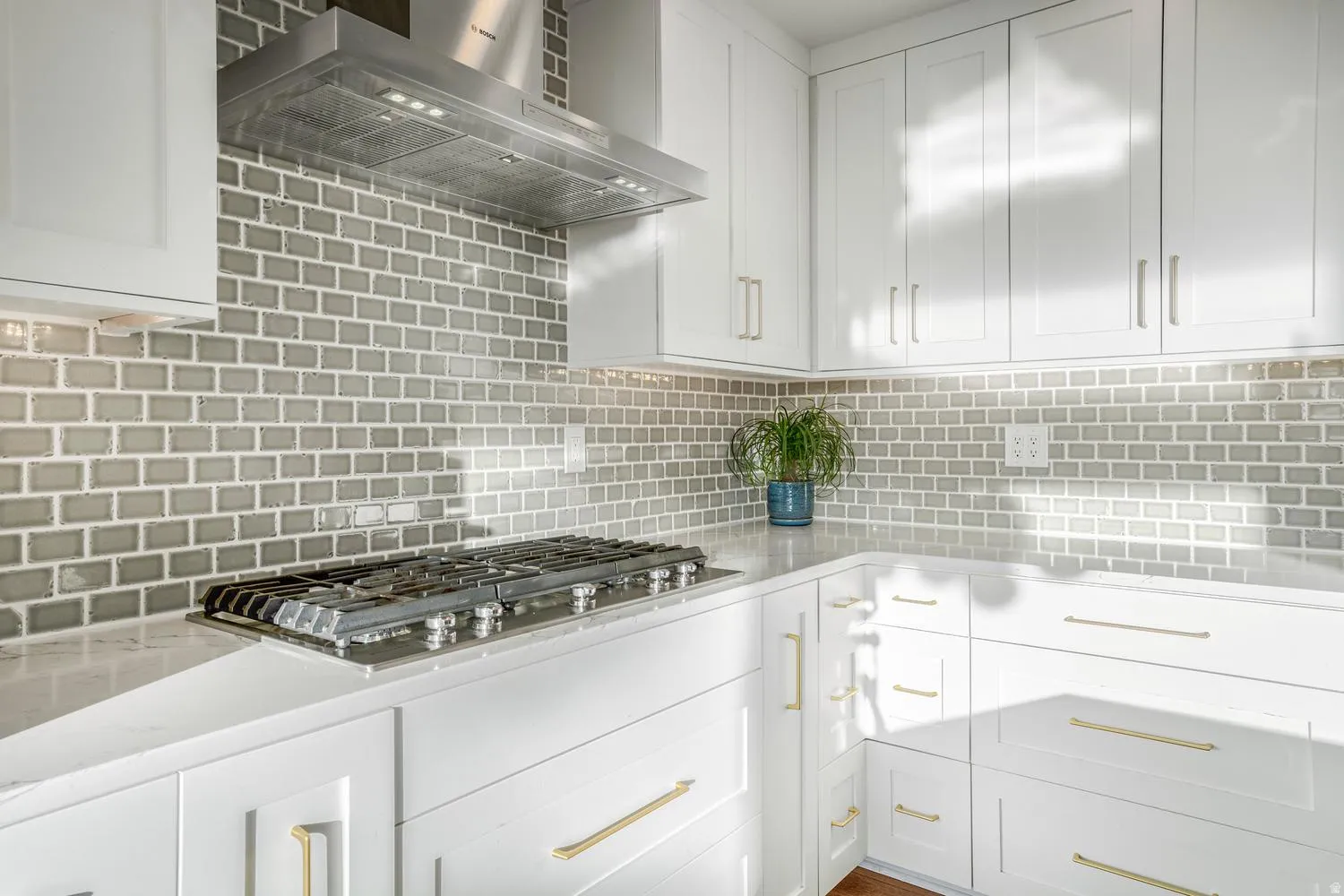 Kitchen featuring a gas range, stainless steel range hood, white cabinetry, light countertops, and a gray subway tile backsplash
