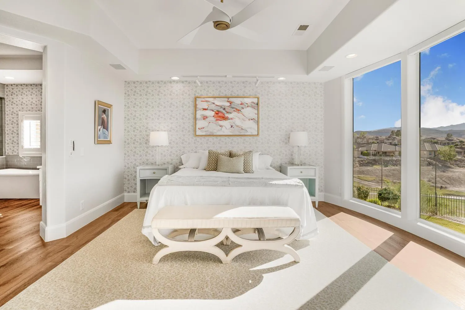 Expansive room featuring wood-finish flooring, a tray ceiling with a ceiling fan, a patterned accent wall, and large picture windows offering a distant landscape