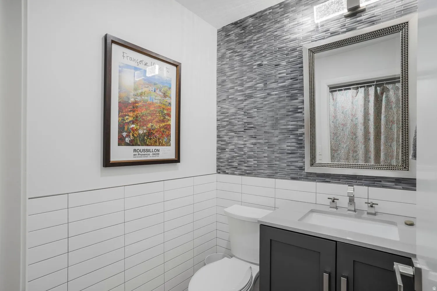 Powder room featuring a dark gray vanity with a light countertop, chrome faucet, and a decorative framed mirror