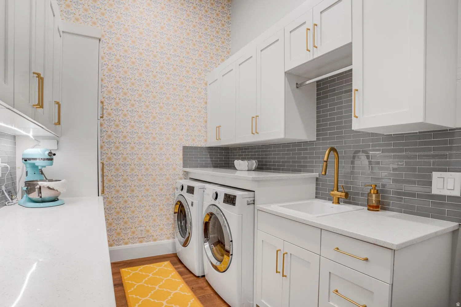 Laundry area featuring white cabinetry with gold-tone hardware, white countertops, and a gray subway tile backsplash