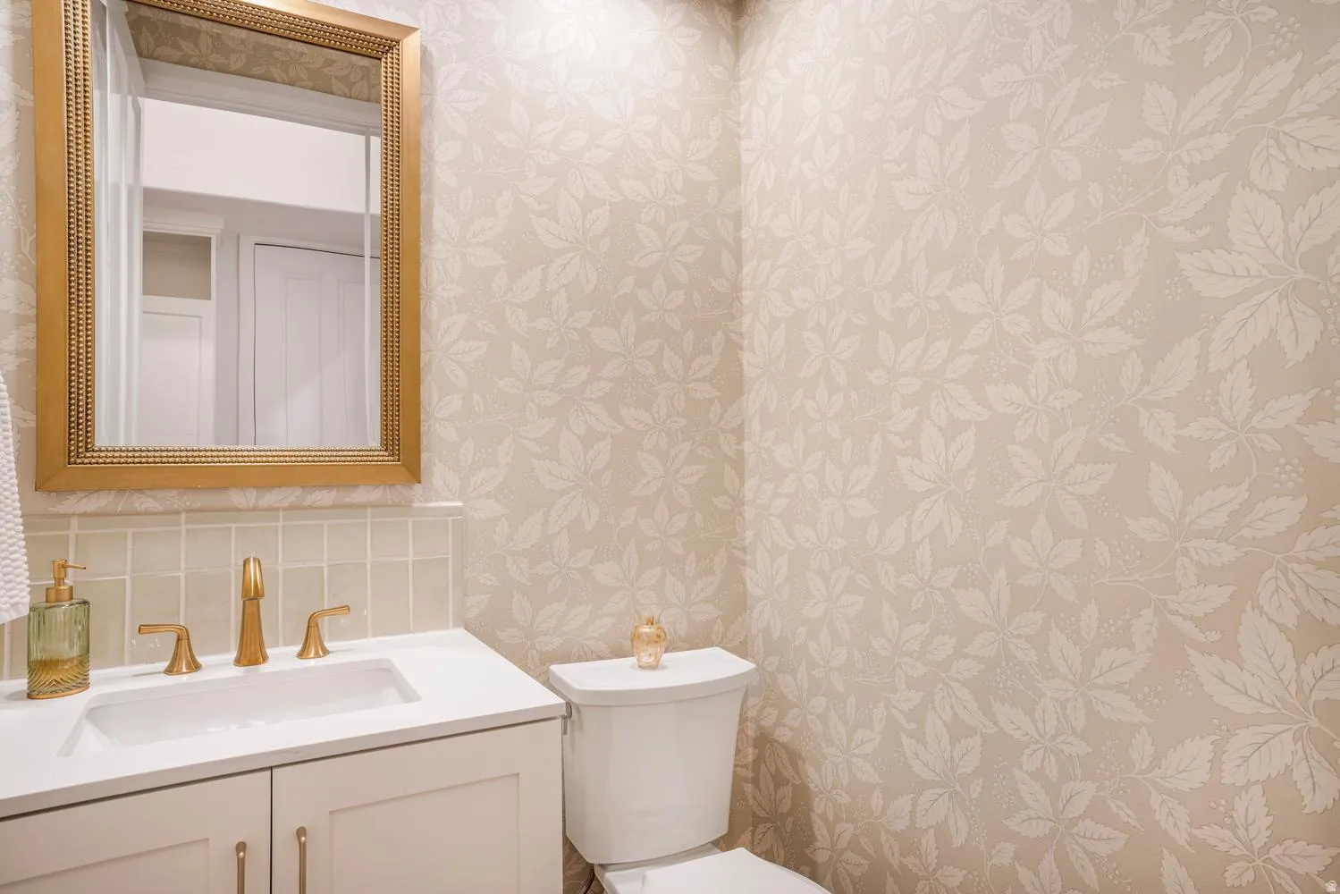 Bathroom featuring a vanity with a white countertop, gold-finish faucet, and a gold-framed mirror