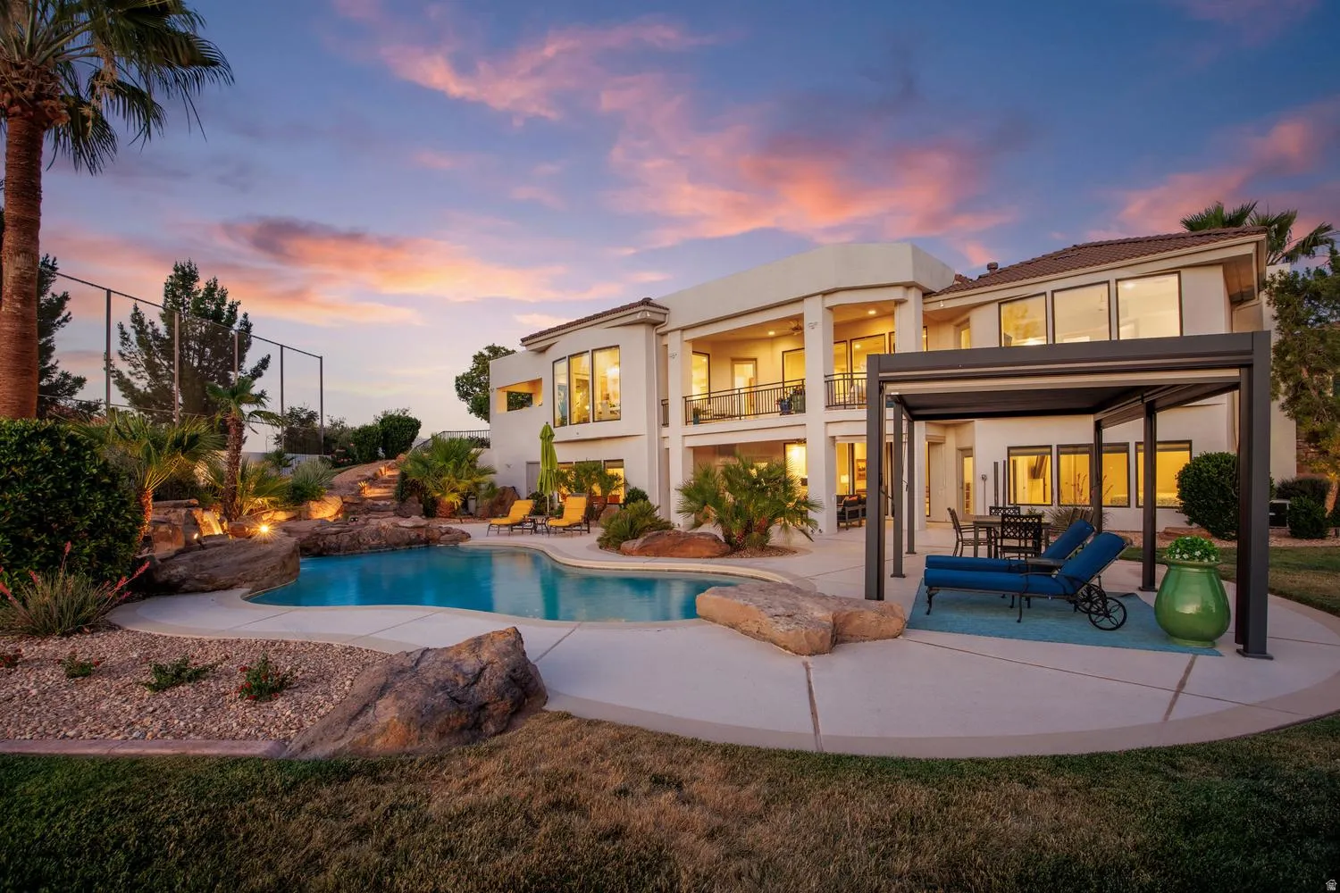 Expansive backyard featuring a large swimming pool with rock waterfall features, mature palm trees, and integrated landscape lighting