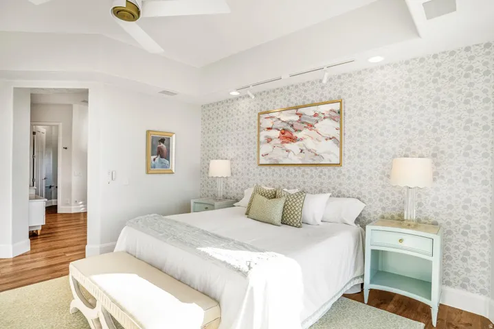 Bedroom featuring patterned accent wall, recessed ceiling with fan, track lighting, and wood-finish flooring