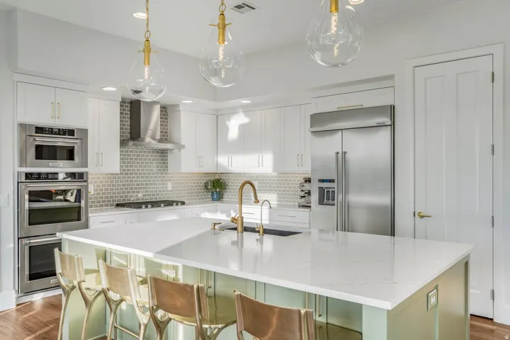Contemporary kitchen featuring a large center island with a light-toned countertop, white cabinetry, integrated stainless steel appliances, a tile backsplash, and decorative pendant lighting