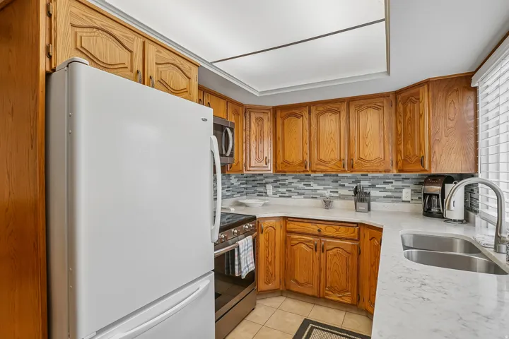 Kitchen featuring wood cabinetry, white countertops, tile backsplash, stainless steel double-basin sink with gooseneck faucet, and tile flooring