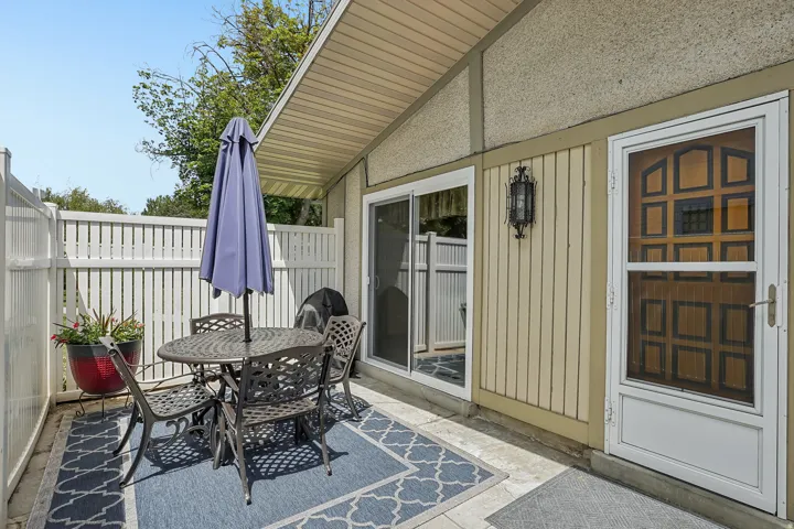 Private patio featuring a white privacy fence, concrete flooring, sliding glass door, exterior lighting fixture, and a paneled entry door with a screen