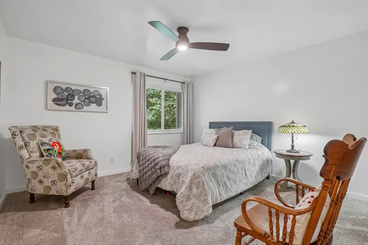 Carpeted bedroom with a window, white walls, and a ceiling fan with integrated lighting