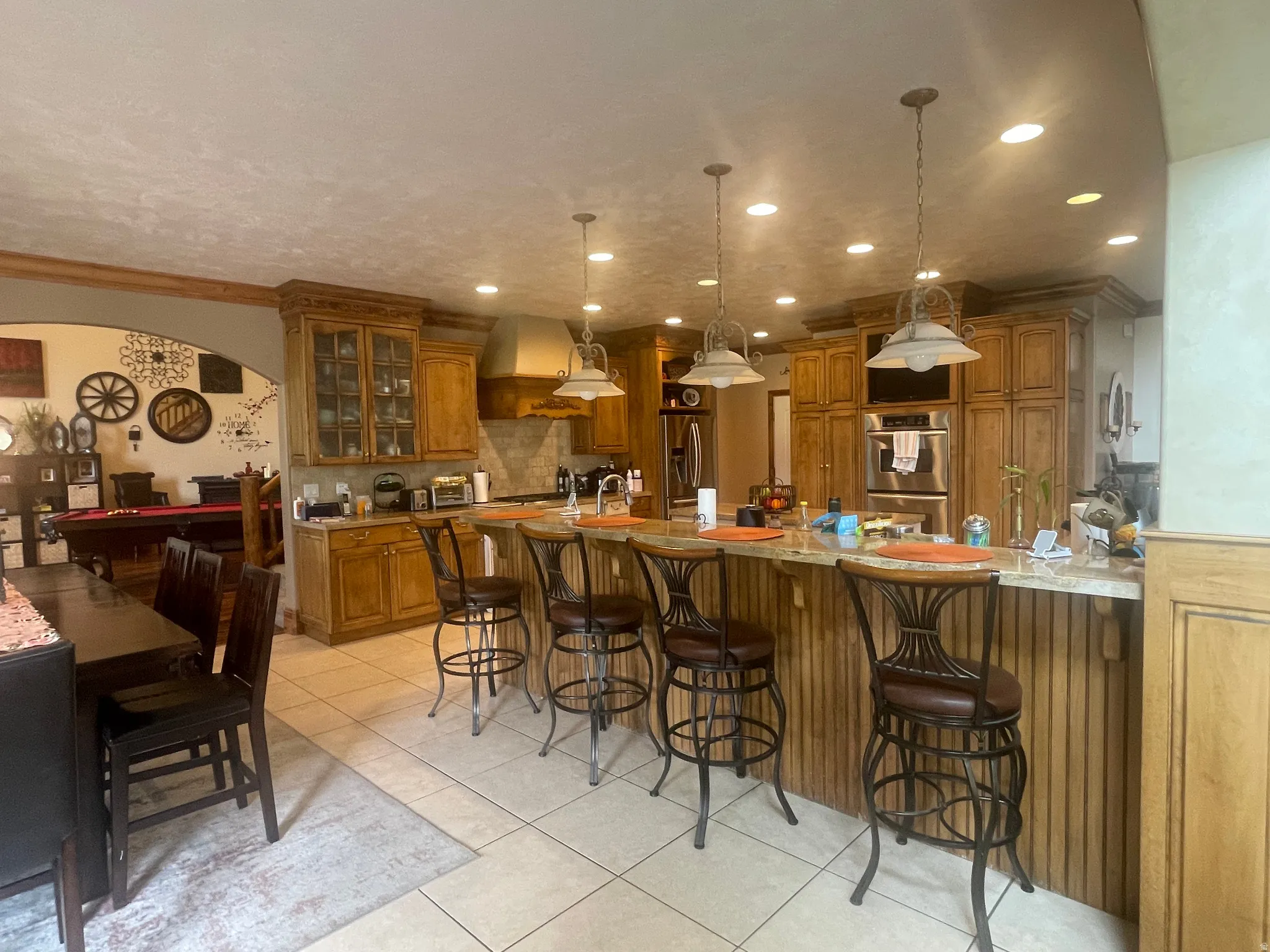 Kitchen featuring a large island with seating, pendant lighting, built-in stainless steel double ovens, custom wood cabinetry, and tile flooring