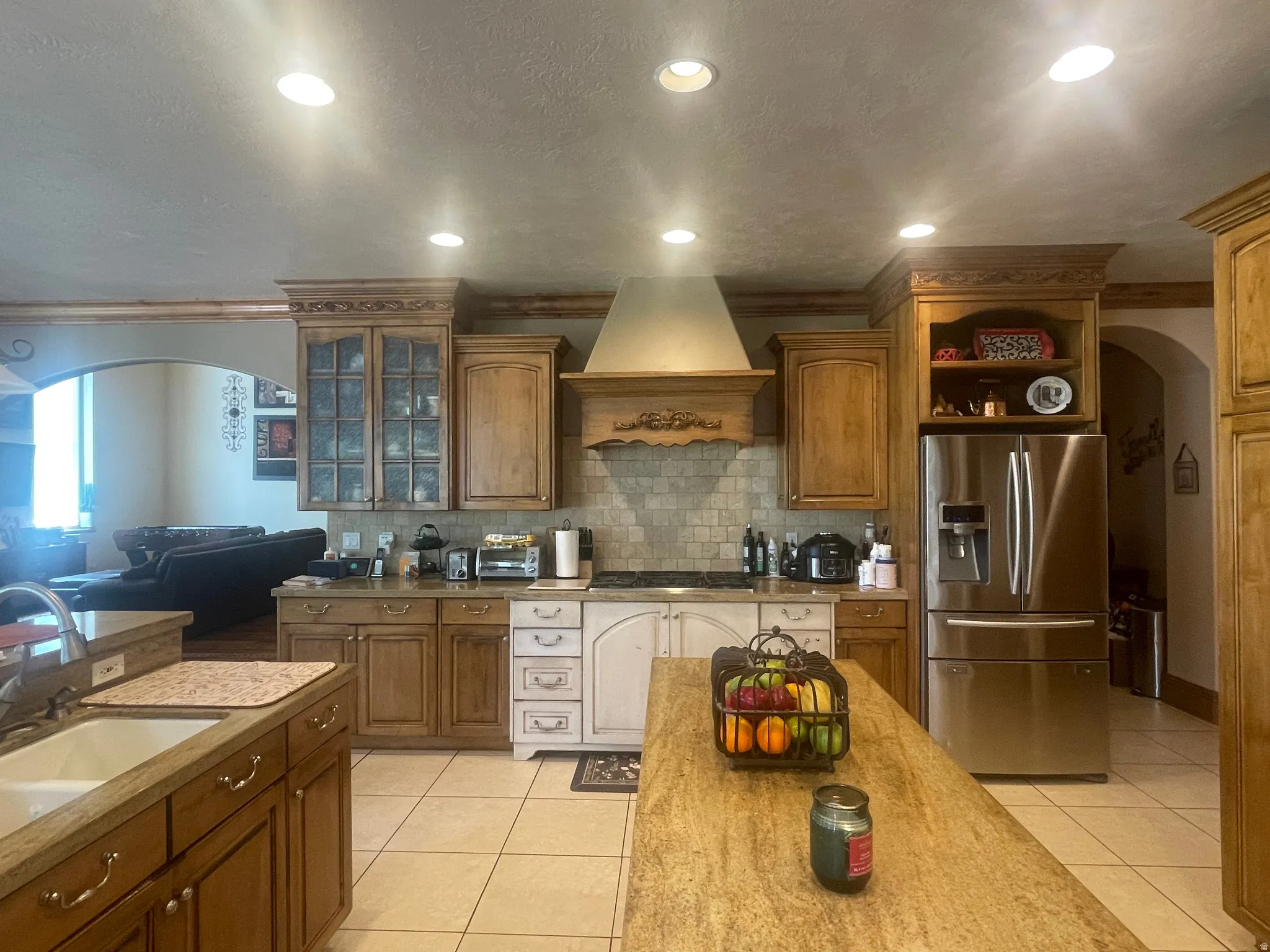 Kitchen featuring a large island with stone-finish countertop, recessed lighting, wood-finish cabinetry, built-in stainless steel refrigerator, and tiled backsplash