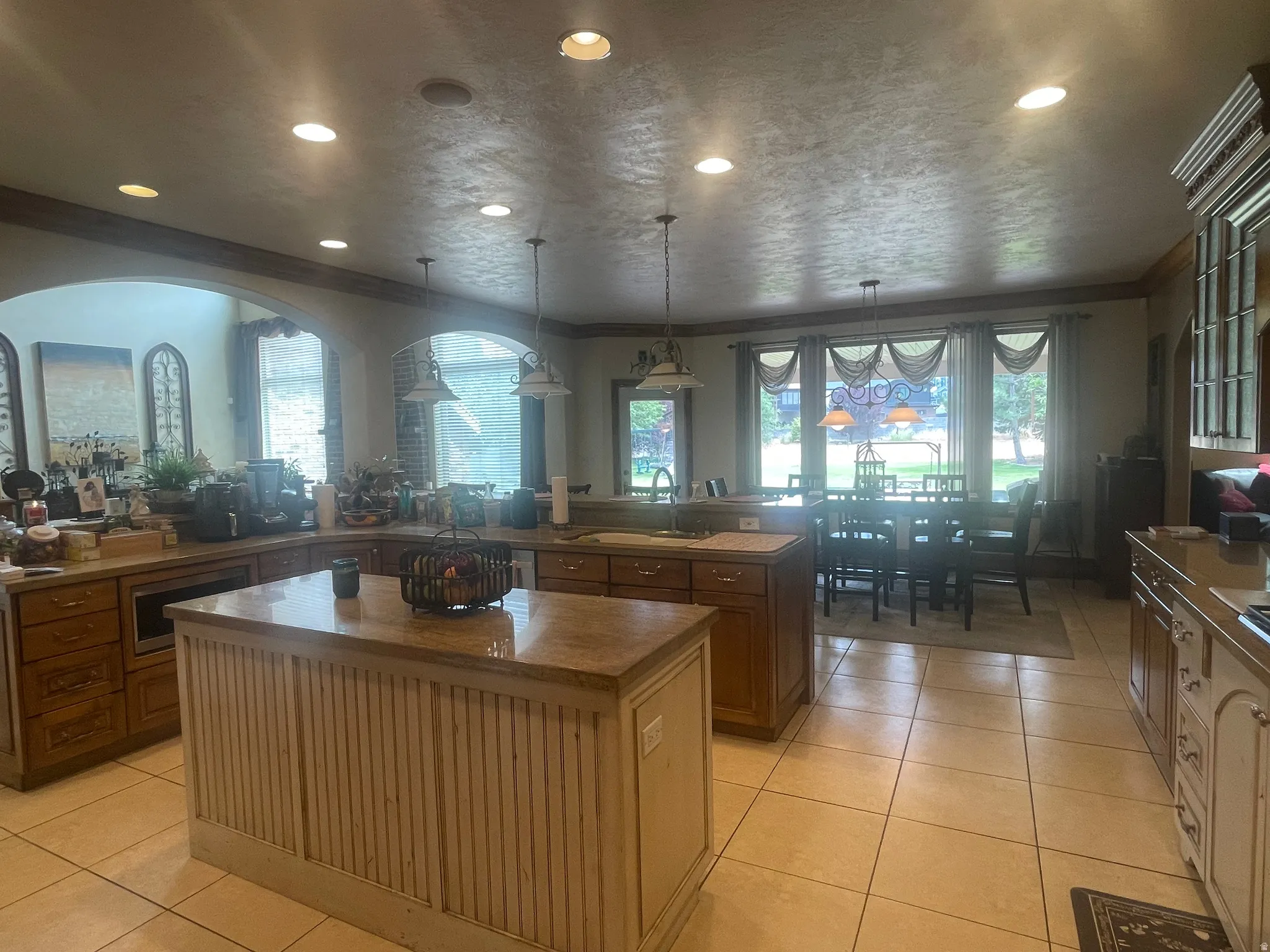 Spacious kitchen featuring a central island with a beadboard base and stone countertop, ample wood cabinetry, recessed lighting, and tile flooring