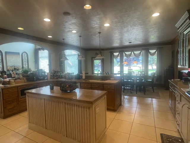 Spacious kitchen featuring a central island with a beadboard base and stone countertop, ample wood cabinetry, recessed lighting, and tile flooring