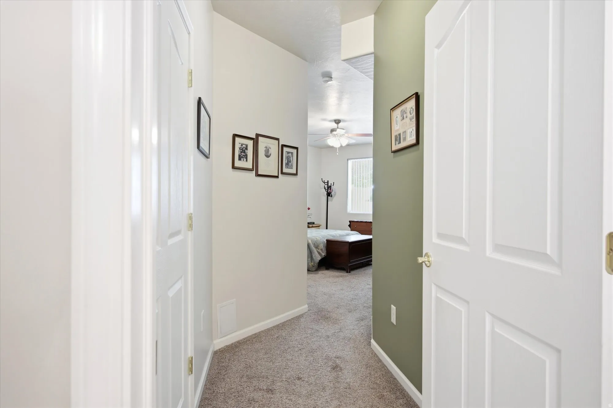 Hallway with light gray walls, a contrasting green accent wall, white baseboards, and textured carpeting