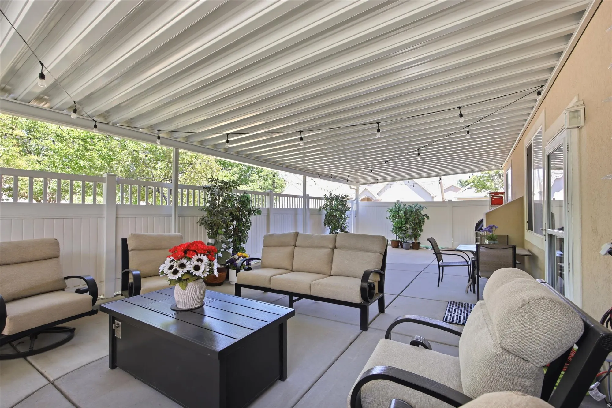 Expansive covered patio featuring string lighting, concrete flooring, and a privacy fence
