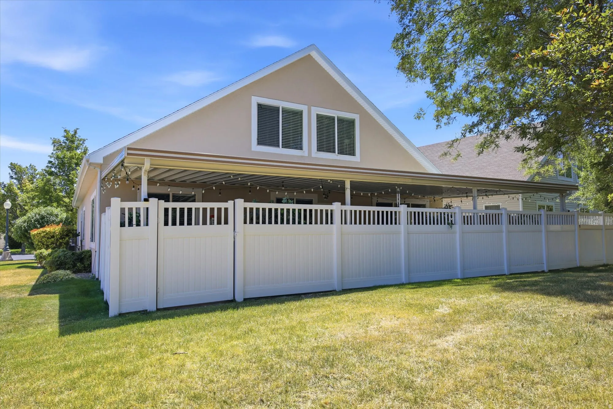 Spacious outdoor patio with overhead awning, string lighting, and a white picket fence