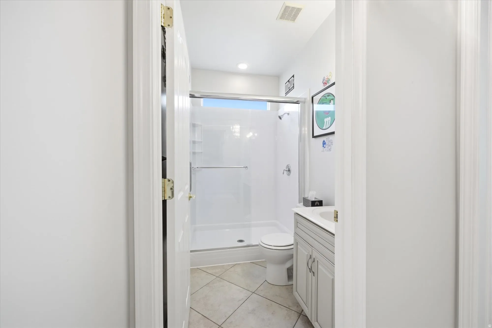 Bathroom featuring a white shower stall with a clear glass enclosure, a white toilet, and a vanity with a light gray cabinet and a white countertop