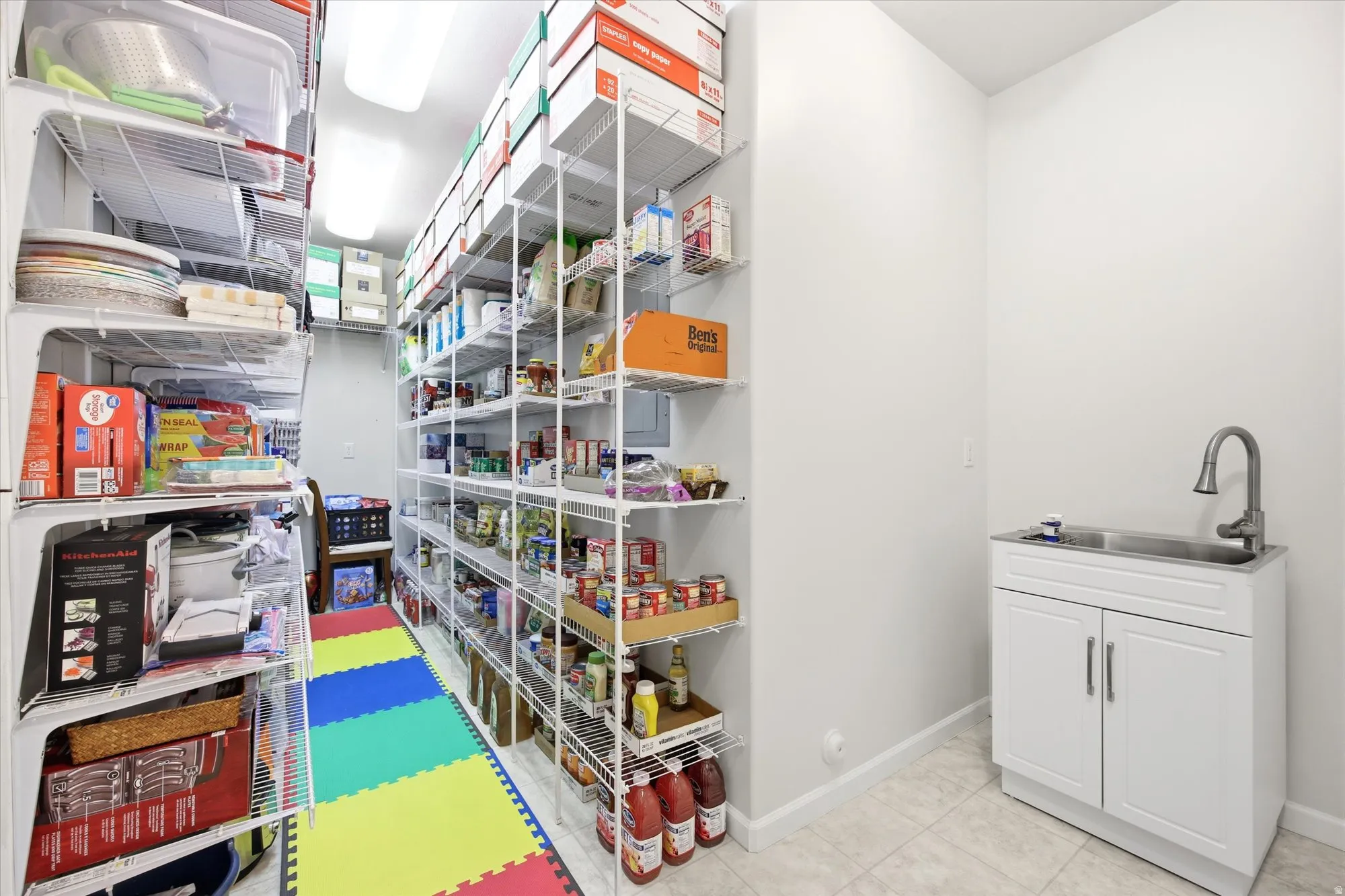 Utility room featuring extensive wire shelving, a white cabinet with a stainless steel sink, and a chrome faucet