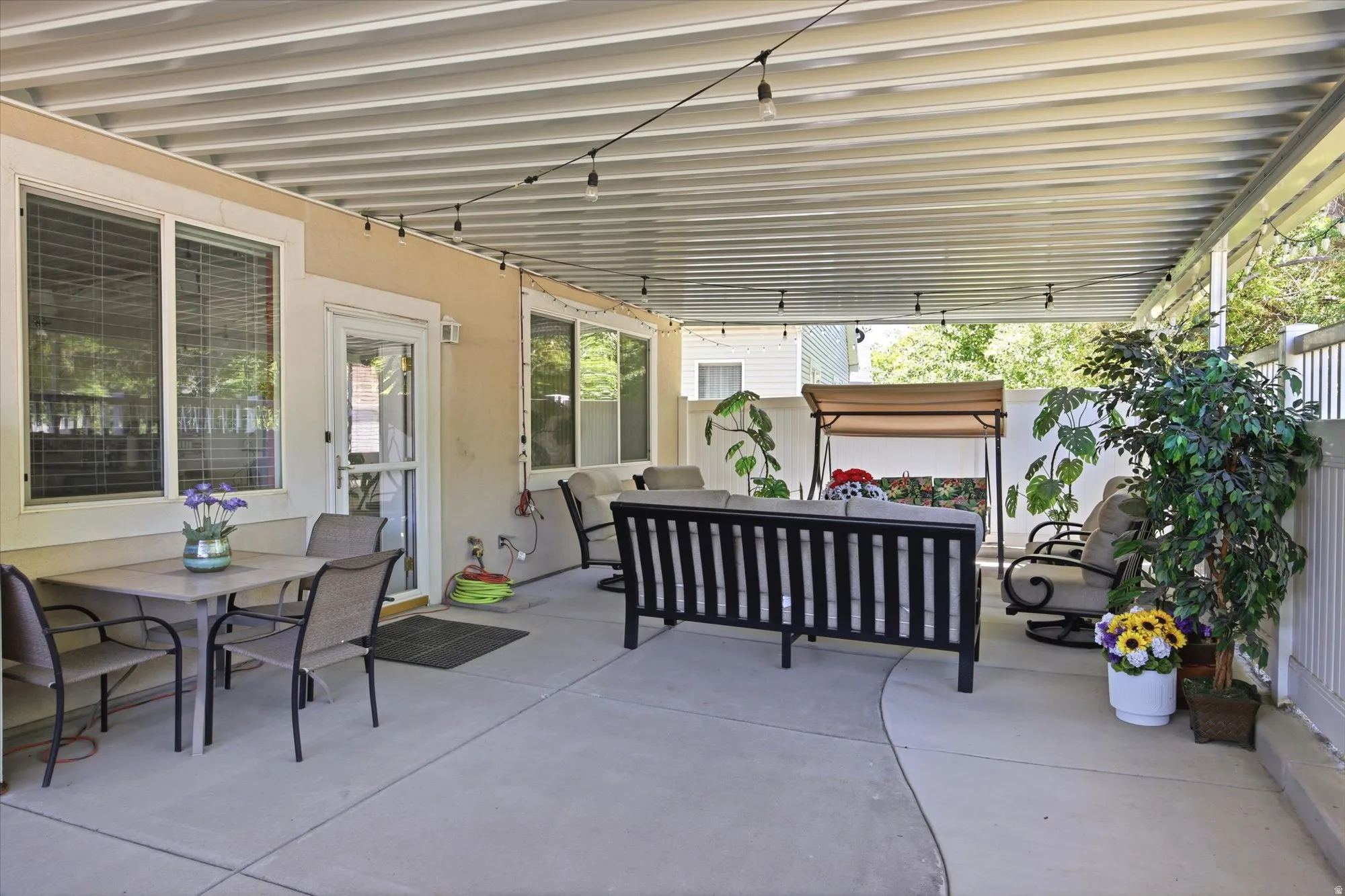 Expansive covered patio featuring string lighting, a concrete surface, and a white perimeter fence