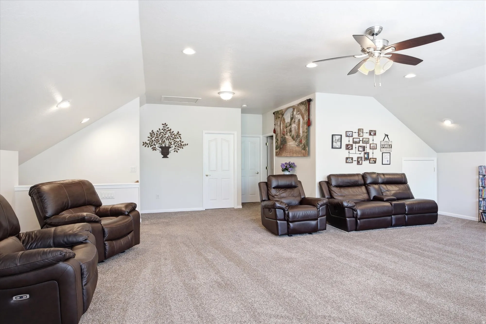 Spacious carpeted room featuring vaulted ceilings, recessed lighting, a ceiling fan, and a painted two-panel door