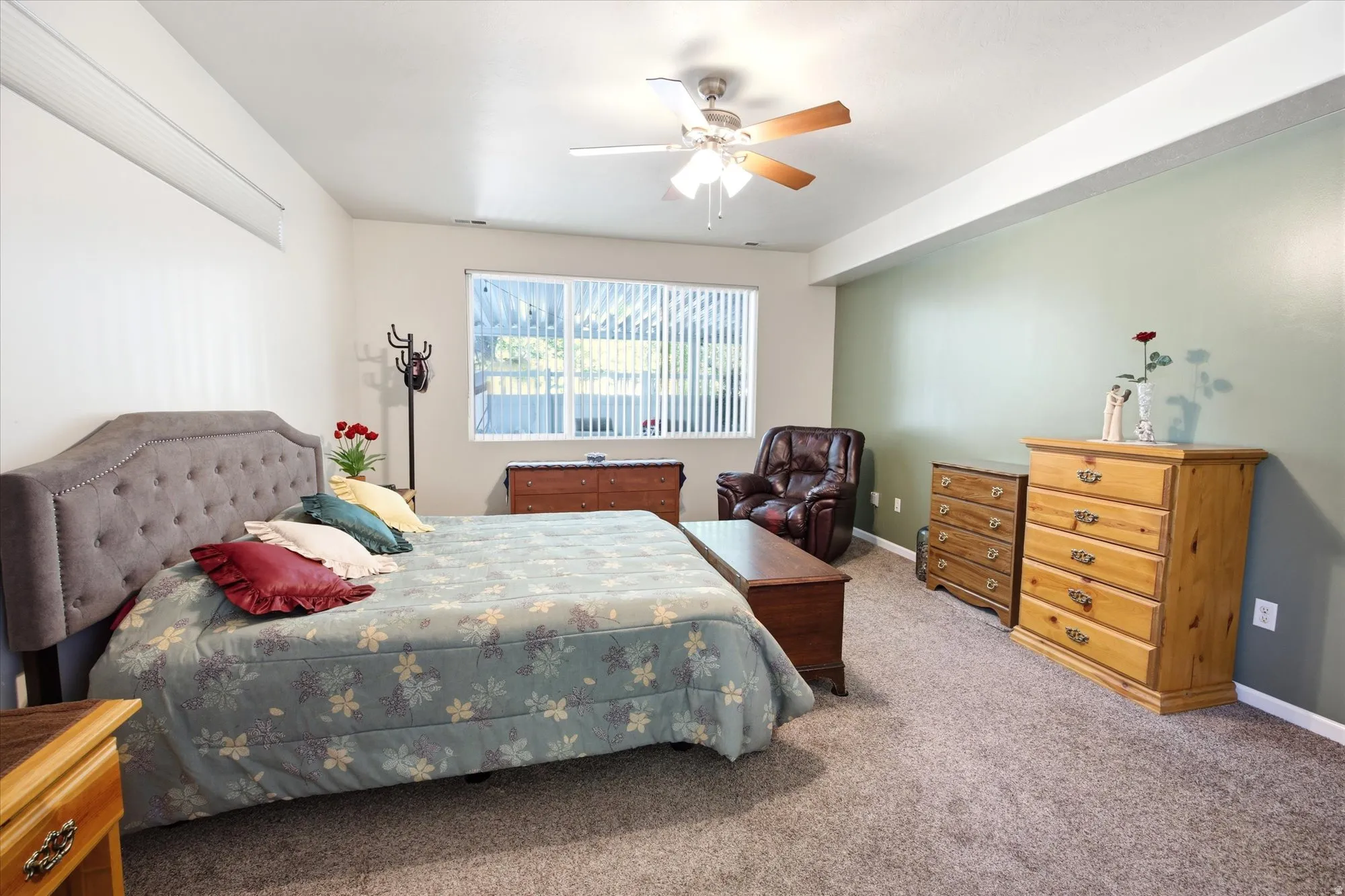 Spacious carpeted room featuring a ceiling fan, a large window with vertical blinds, and a light green accent wall