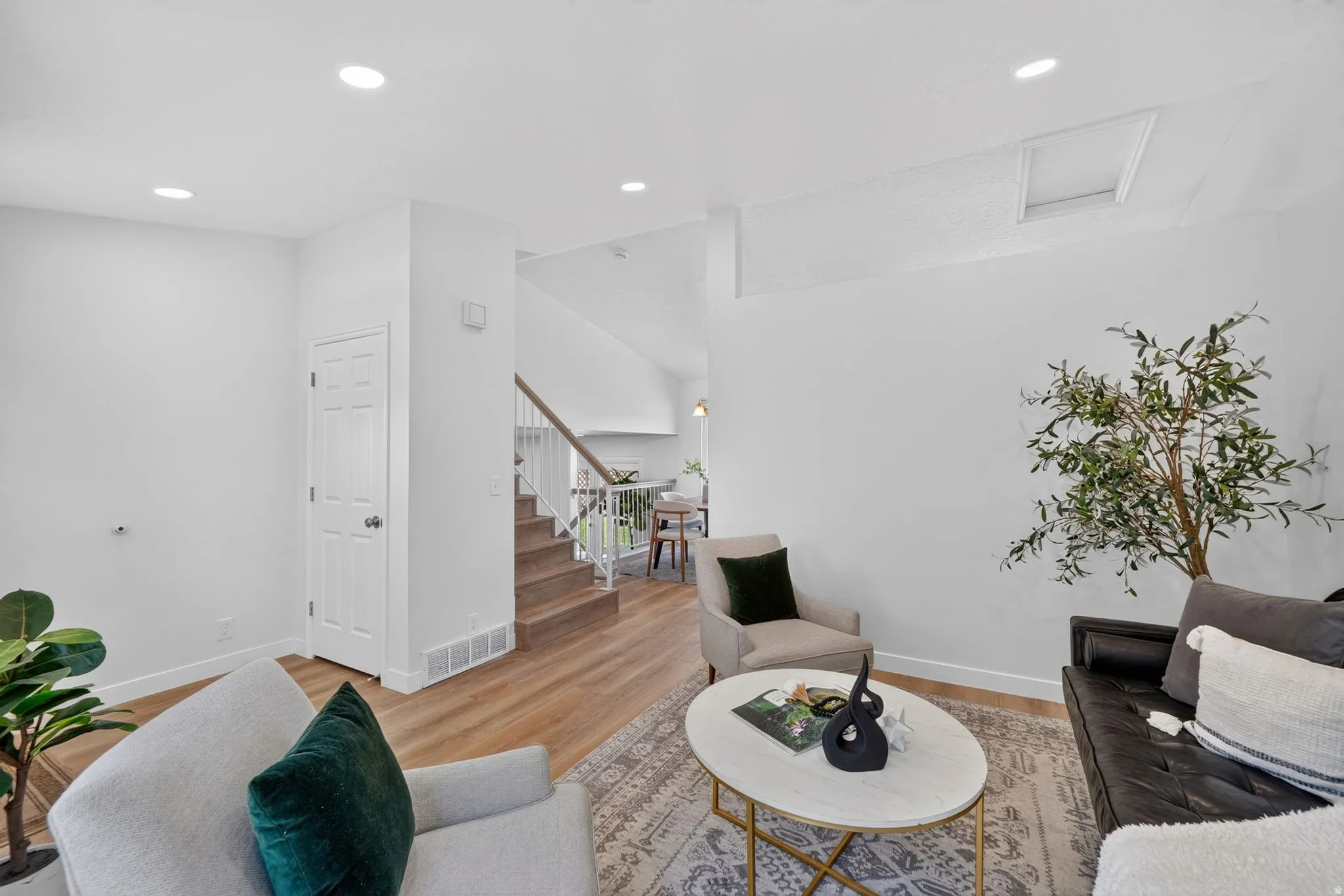 Spacious living area featuring light wood-finish flooring, a contemporary staircase with white risers and a wood handrail, recessed lighting, and crisp white walls