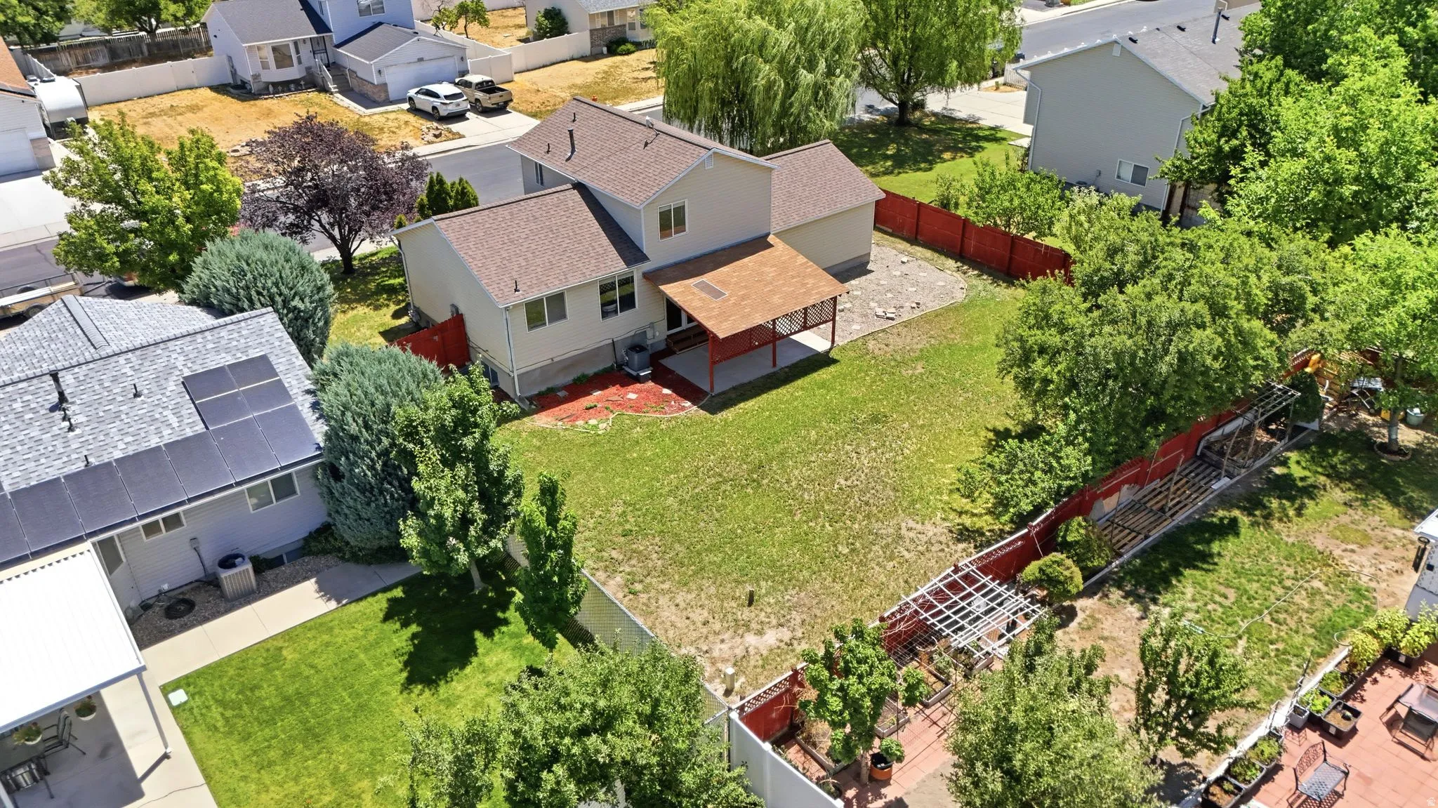 Expansive rear yard featuring a large patio cover, mature trees, and a red perimeter fence