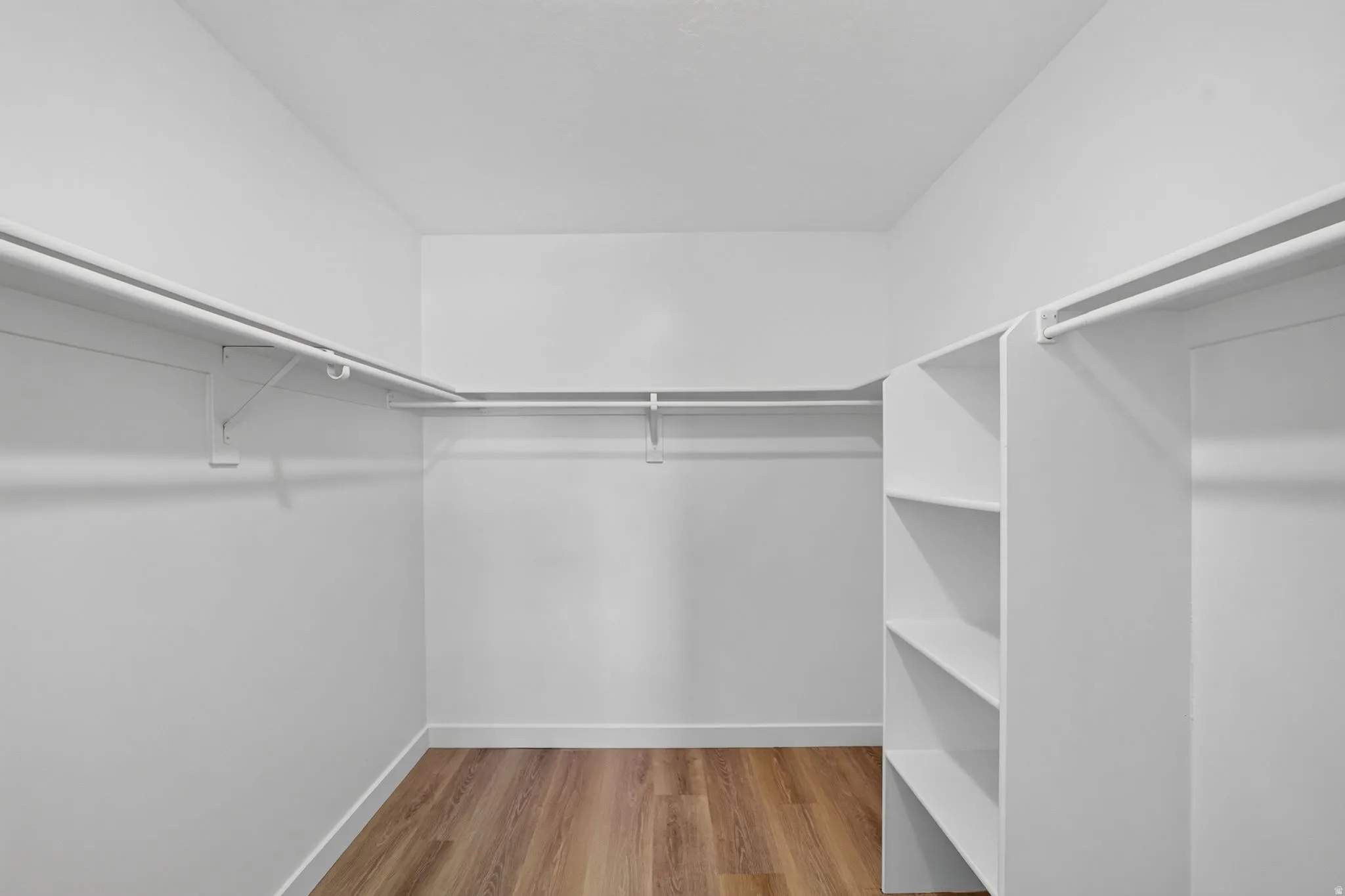 Walk-in closet featuring wood-finish flooring, white walls, built-in shelving, and multiple clothing rods