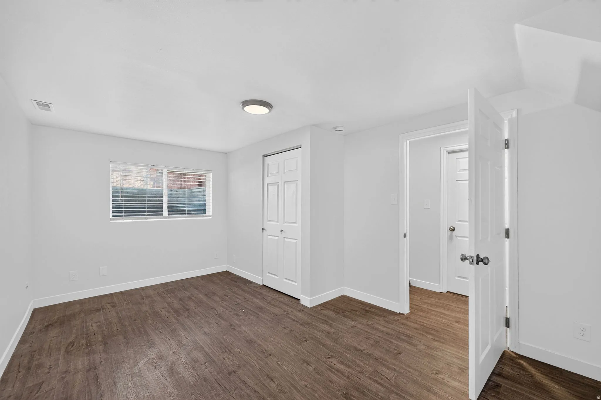 Room featuring wood-finish flooring, white walls, and a window with horizontal blinds