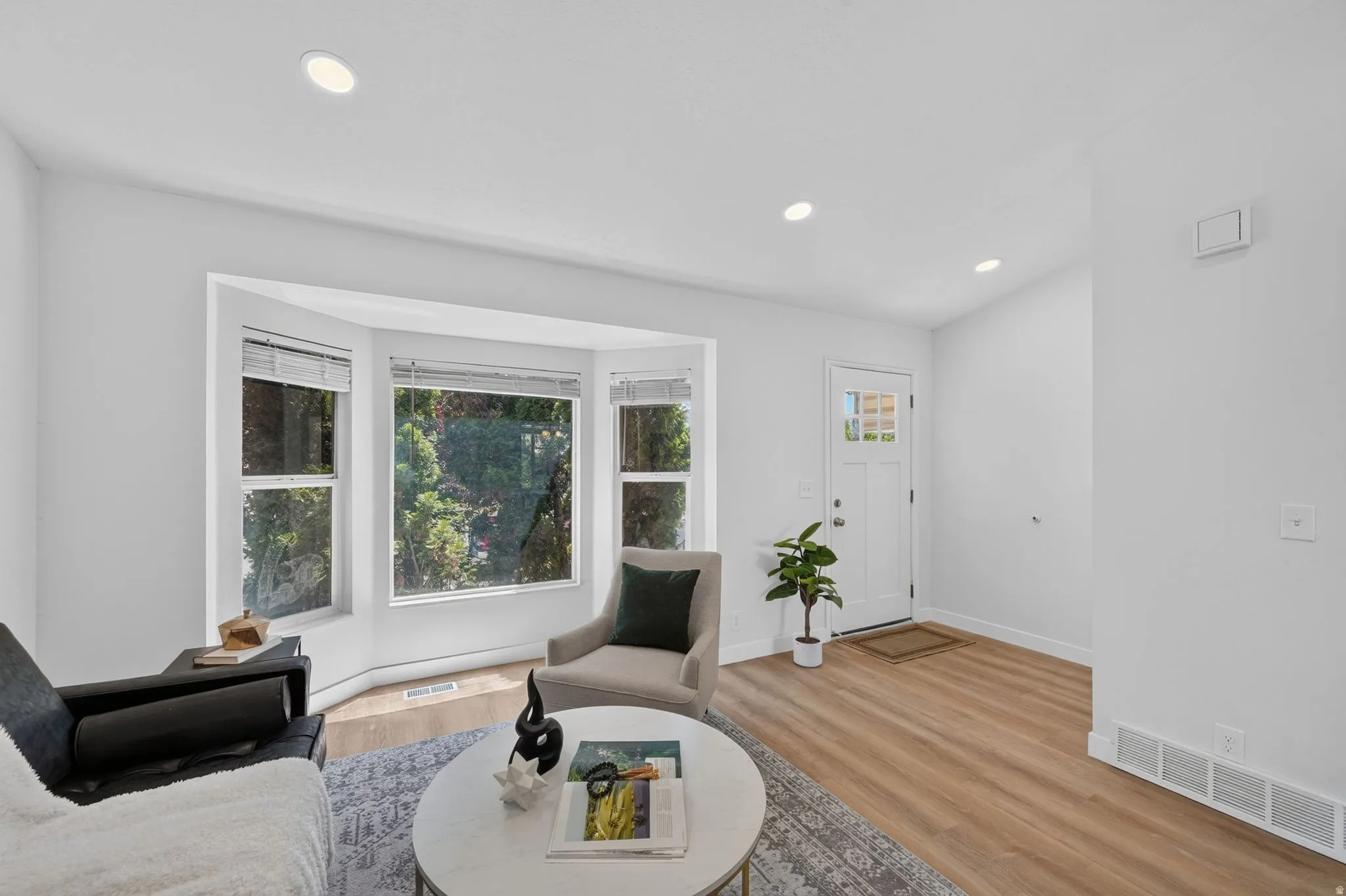 Living area featuring a bay window with multiple panes, wood-finish flooring, recessed lighting, white walls, and a front entry door with decorative glass inserts