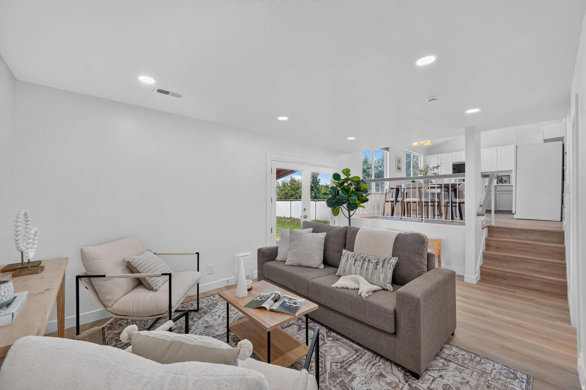 Open-concept living area featuring light wood-finish flooring, recessed ceiling lighting, and a partial wall with a railing overlooking the kitchen